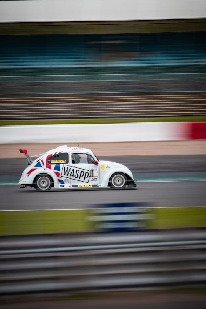 services-01 A Volkswagen Beetle racing on an English track, showcasing speed and motion in motorsport.