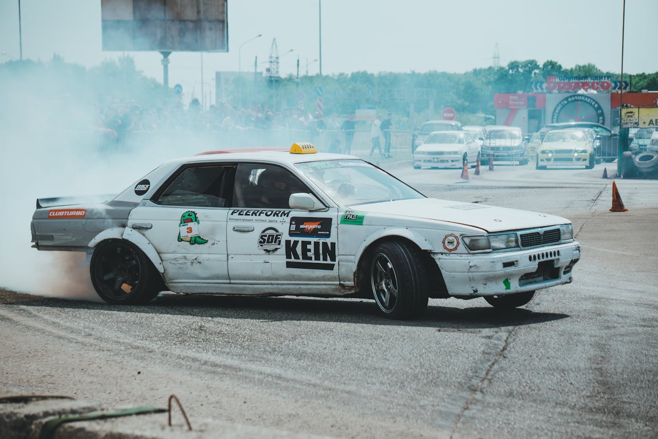 White sports car drifting on track with visible smoke, showcasing automotive skill and modifications.